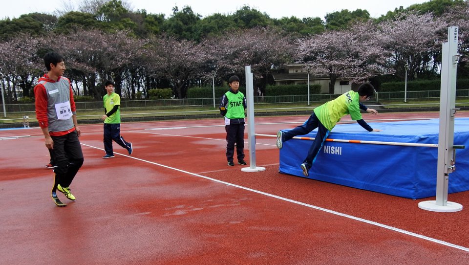 【「SRCアスリート・スポーツ交流会」で、走り高跳びに挑戦する子どもたちを見守る義足のジャンパー鈴木徹選手(左)=2016年4月2日/千葉市内】