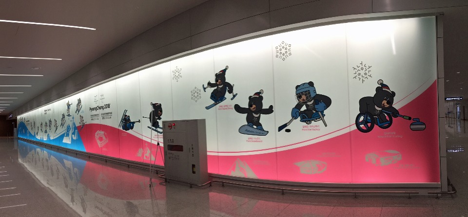 韓国・仁川国際空港に設置されている、「PyeongChang 2018」大会PR用のディスプレイ。手前のピンクの部分は、パラリンピックのマスコット「バンダビ(ツキノワグマ)が実施される6競技に挑戦! 奥の水色部分ではオリンピックのマスコット「スホラン(白虎)」がオリンピックの15種目を紹介。